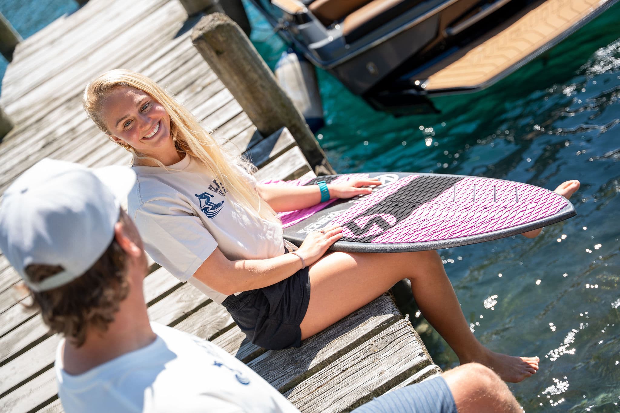 Coach Emma Galusha on the jetty with a skim-style wakesurf board across her lap