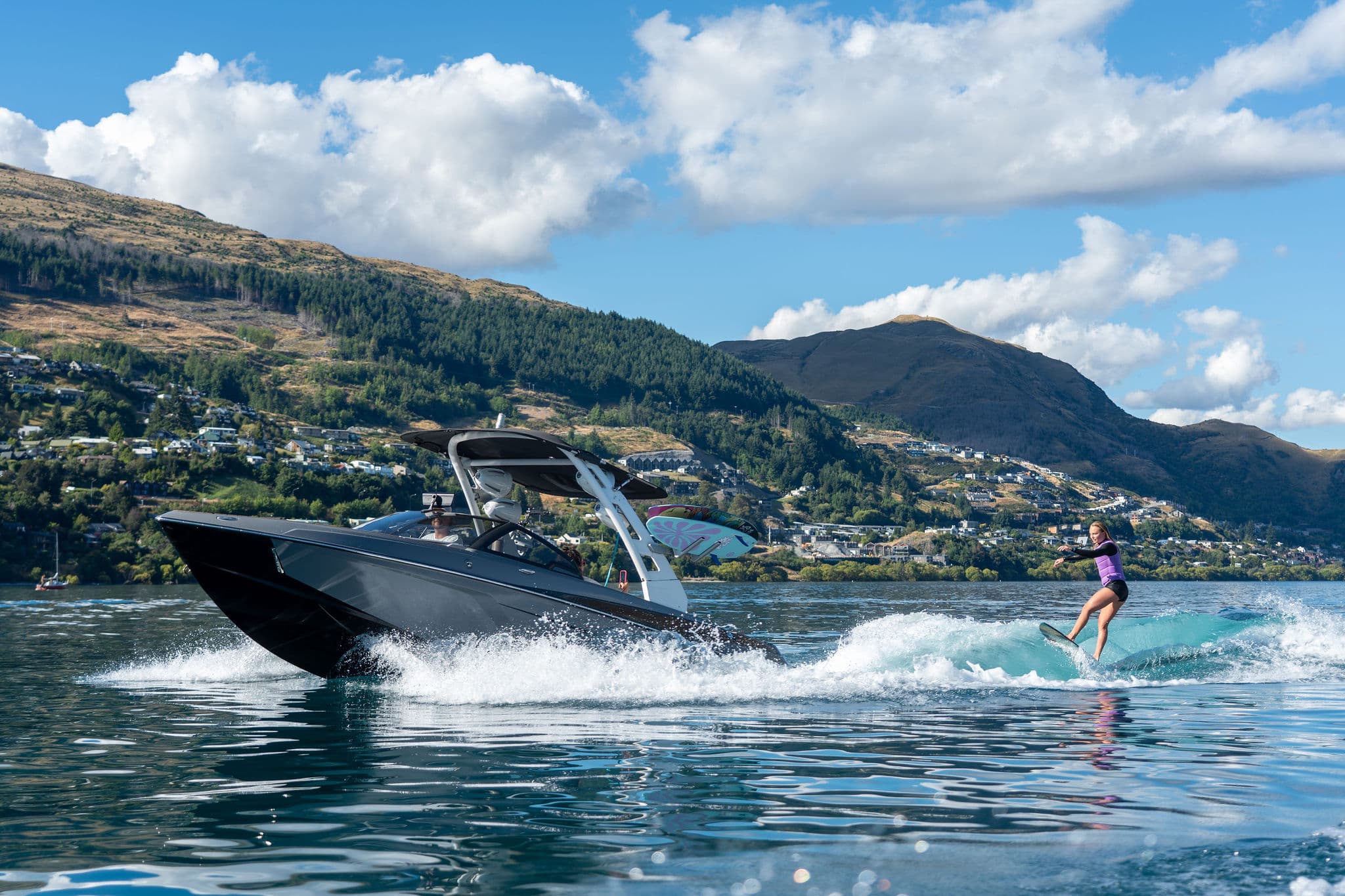 Wake boat towing a wakesurfer on a clean wave, mountains behind